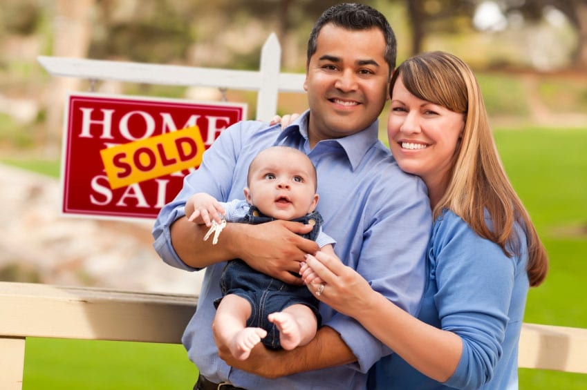 couple with a baby in front of a home with a sold sign