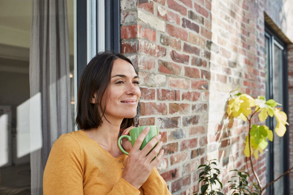Woman standing on the patio of her new brick home with coffee
