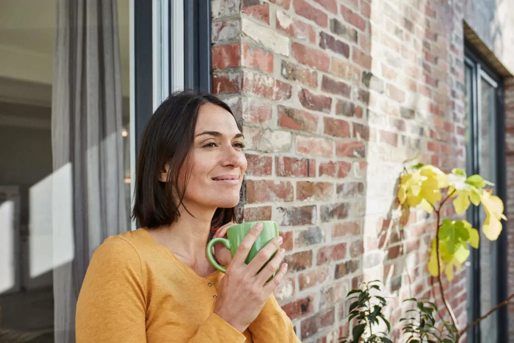 Woman standing on the patio of her new brick home with coffee