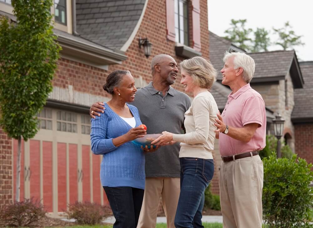 Two senior couples greeting each other in front of a home