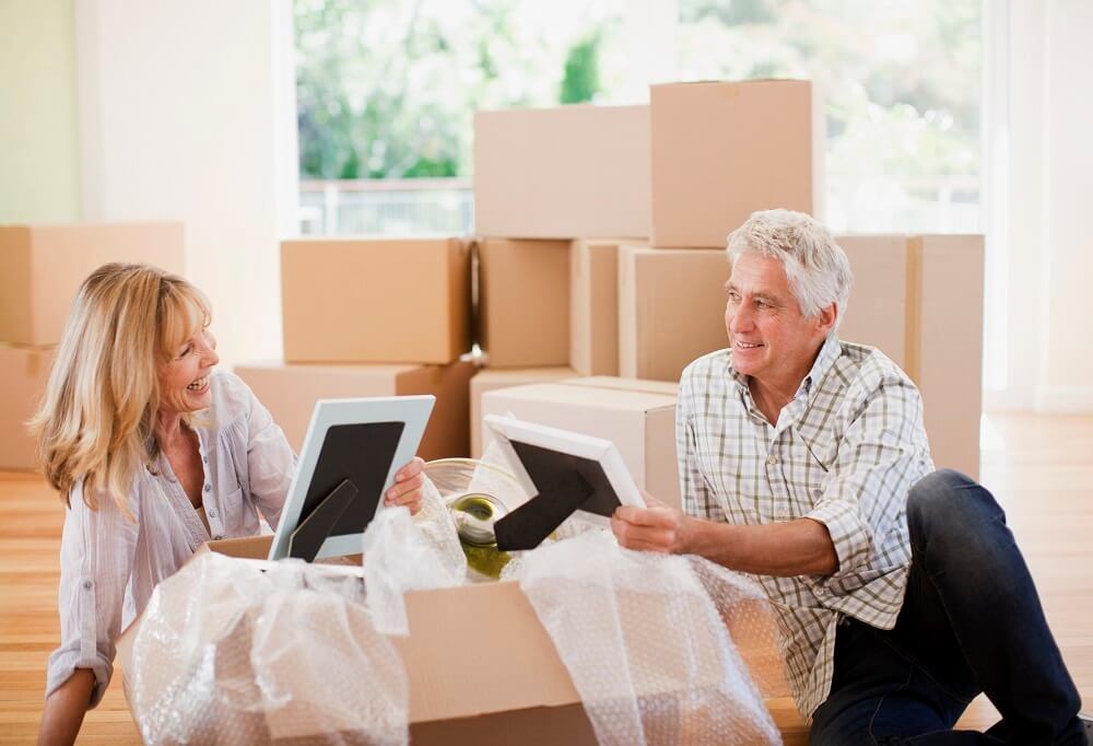 Senior couple sitting on the floor unpacking pictures in new home