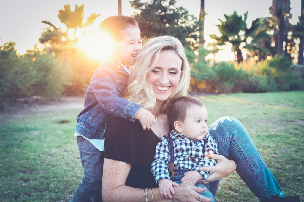 woman holding baby sitting on green grass field under sunset