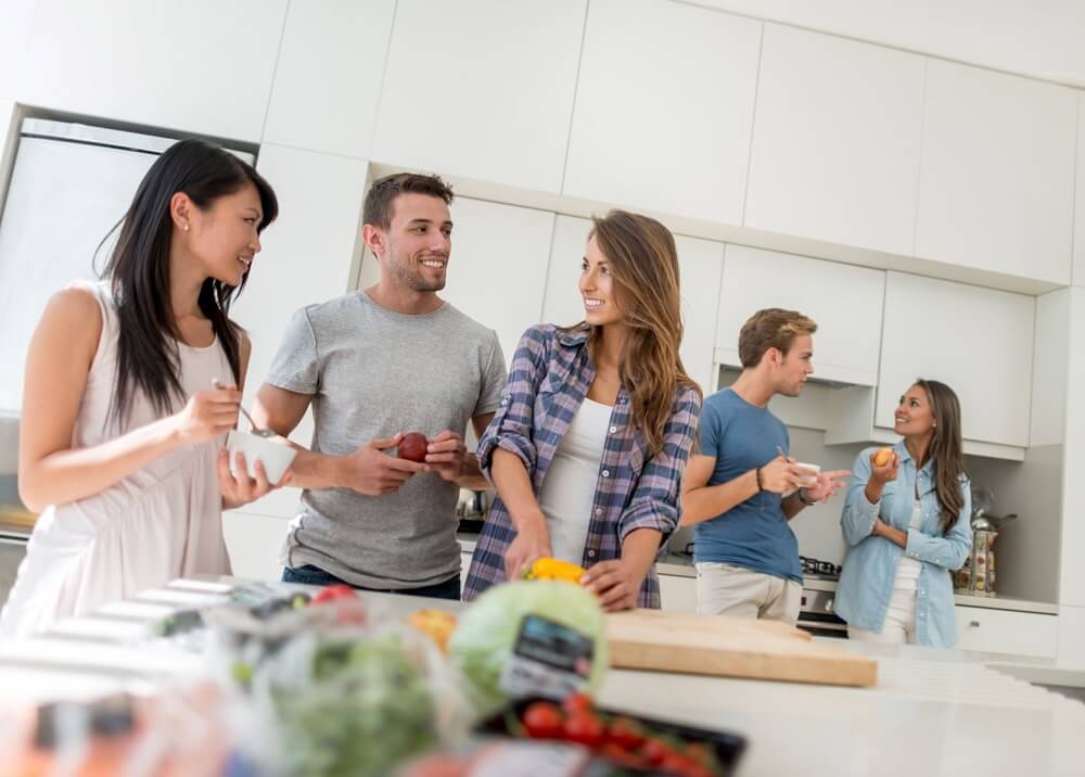 A group of millennial friends in the kitchen preparing food and chatting