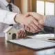 Men sitting at desk shaking hands over a house contract
