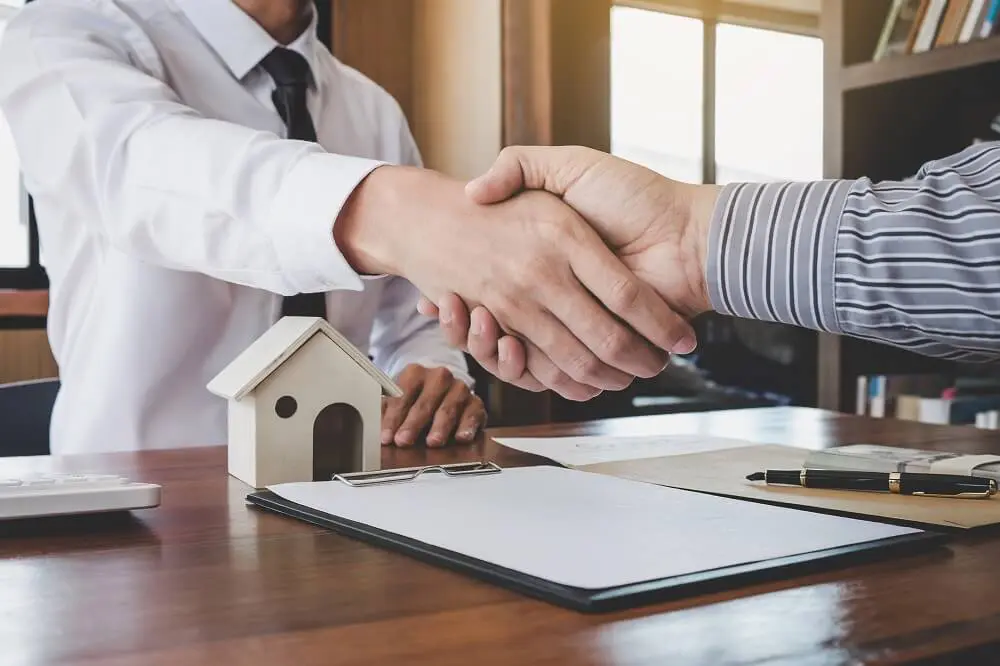 Men sitting at desk shaking hands over a house contract
