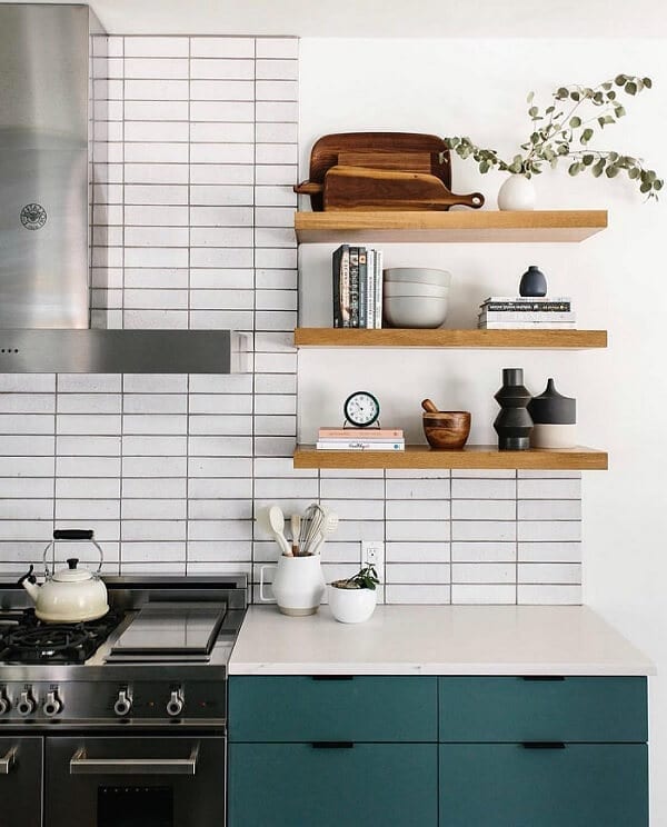 Kitchen with white stacked tile backsplash, green cabinets, and wooden floating shelves