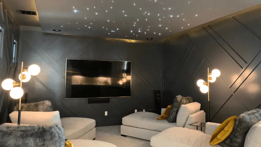 A home theater with several chaise lounges, dim lamps, and a ceiling that mimics a starry sky.