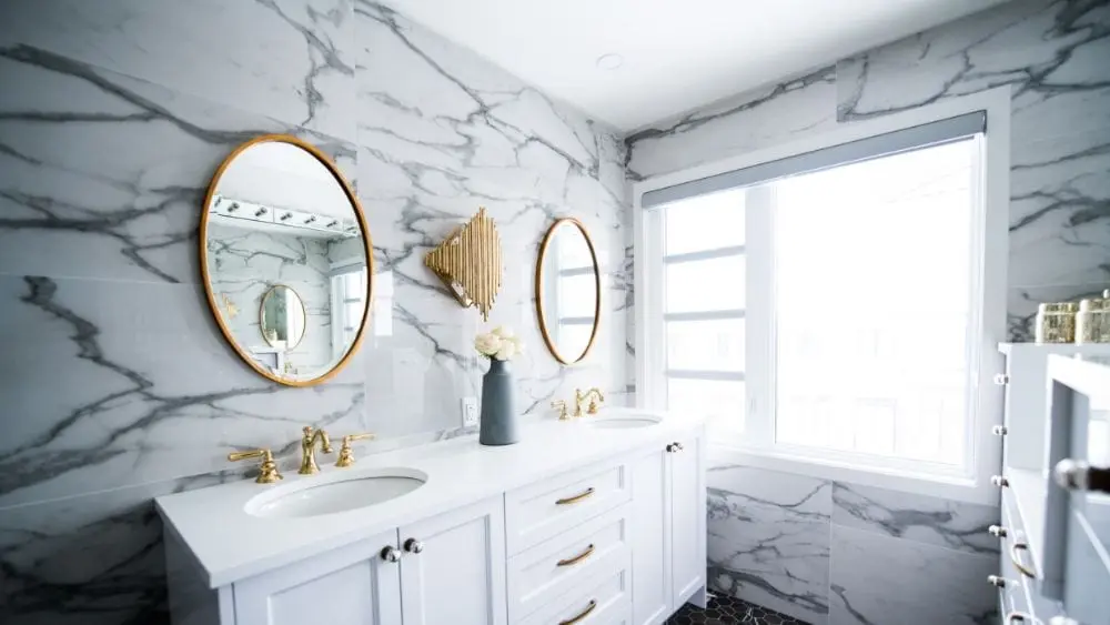 Bathroom with marble walls, white furniture, and gold accents.