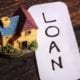 A small, colorful house figurine next to a strip of paper with "loan" written on it in marker.