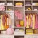 An organized closet with yellow and pink clothes hanging on rods or folded on shelves