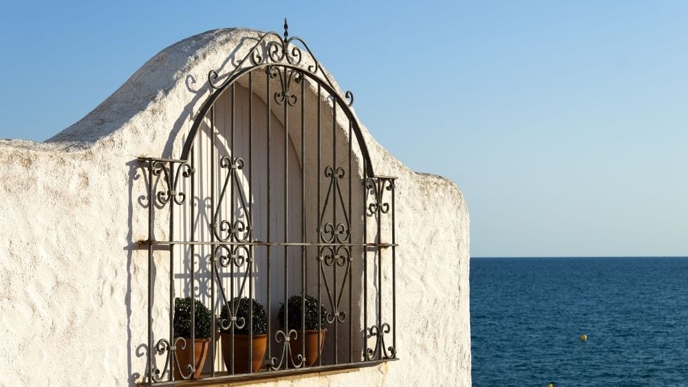 A textured stucco with an archway cut into it. Planters sit on the edge and a wrought iron gate covers the opening.