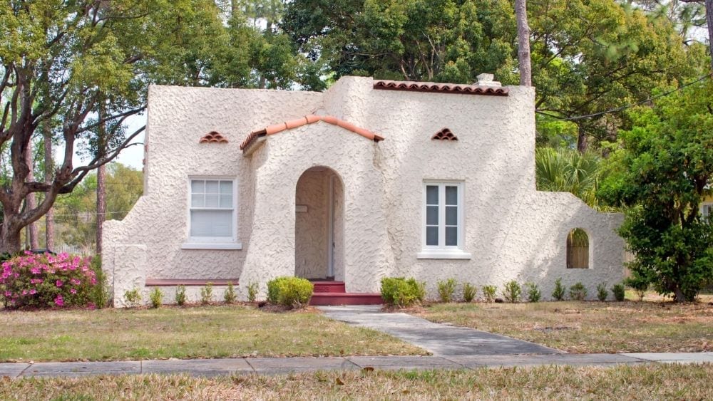 A smaller Spanish-style house with textured stucco walls and a small awning over the front door with a barrel roof.