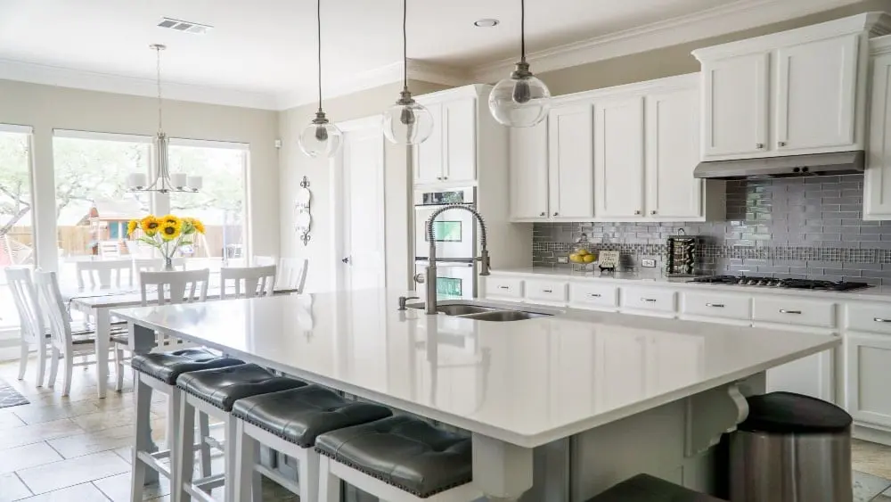 A new kitchen featuring white cabinets, an island with white quartz countertop and breakfast nook with large windows