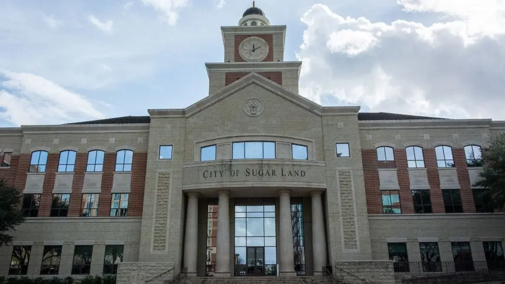 Stately building made of bruck with a clock tower and a dome at the top. Above the door reads, "City of Sugar Land."