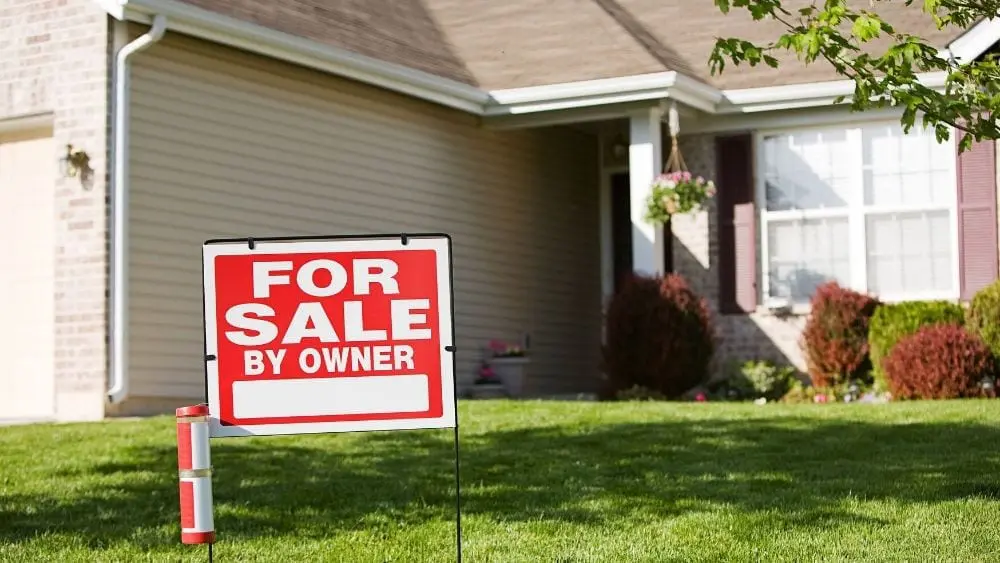 A home with a clean lawn and a "For Sale By Owner" sign.
