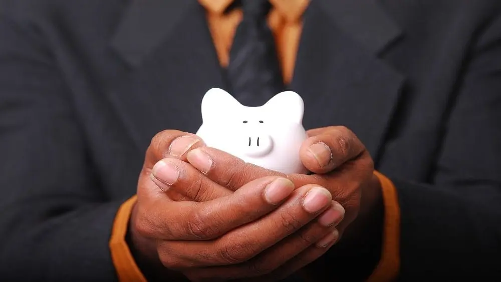 Man in suit holding a white piggy bank.