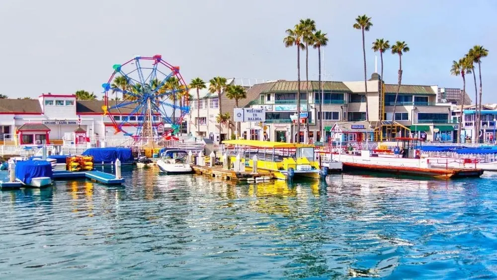 View from the water of a pier with colorful boats docked and a Ferris wheel on the pier.