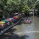View of the San Antonio River in San Antonio Texas with a riverboat filled with tourists on the water and brightly colored umbrellas lining the River Walk on the left