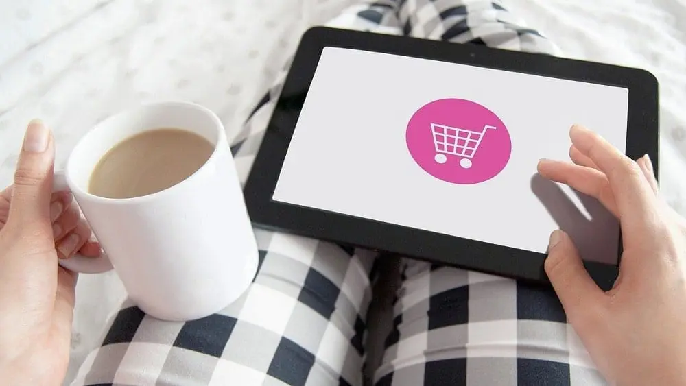 Person with cup of coffee shopping online via tablet.