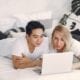 Couple lying on bed looking at laptop.