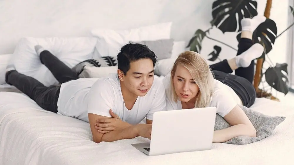 Couple lying on bed looking at laptop.