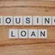 Letter blocks lying on wooden table that spell out "HOUSING LOAN".