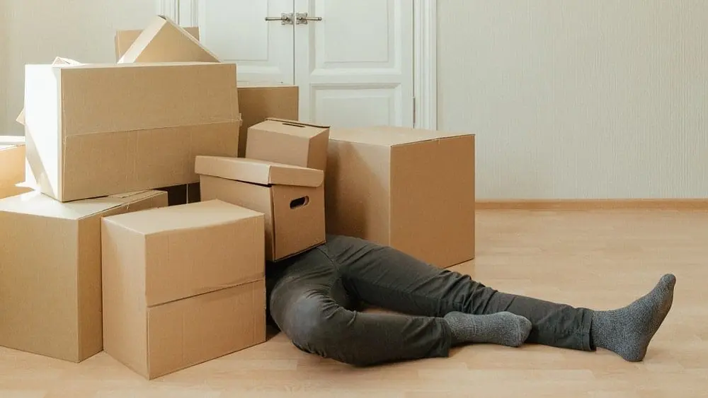 Person lying underneath a pile of cardboard boxes with only their legs showing.