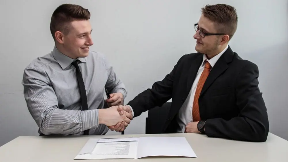 Two people sitting at desk over documents and shaking hands.