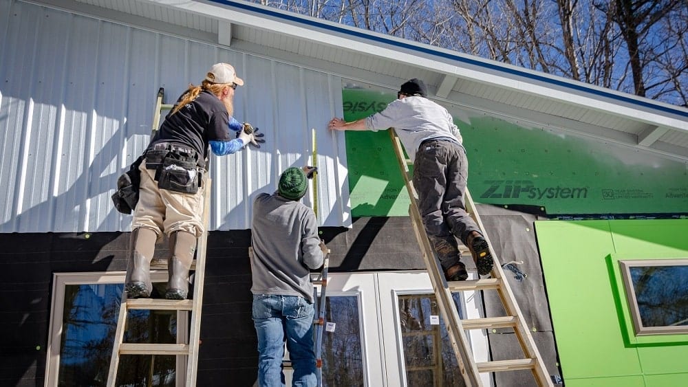 Three people on ladders building a house.