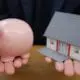 Person holding pink piggy bank in one hand and a miniature house in the other.