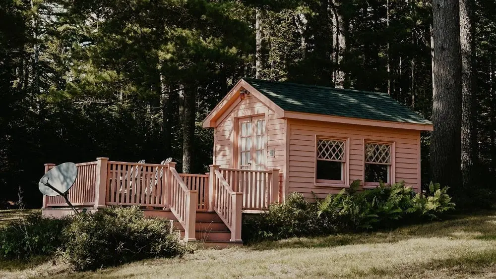 Small pink wooden house with patio in the woods.
