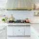 White and gold kitchen with subway tile backsplash, marble countertops, and open shelving.