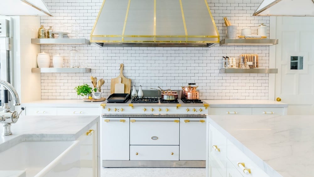 White and gold kitchen with subway tile backsplash, marble countertops, and open shelving.