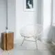 White interior with white chair, wooden side table and concrete-like flooring.