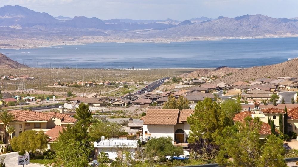 View of a suburb with Spanish-style homes. A lake and mountain range sit in the background.
