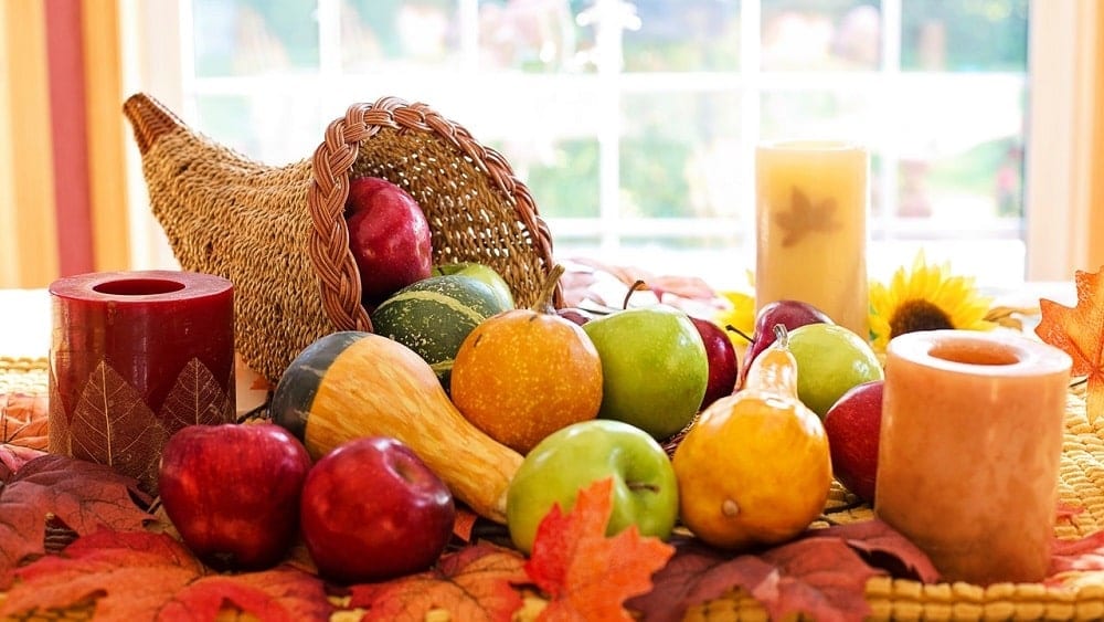 Table set with fall candles and a cornucopia overflowing with apples and gourds.
