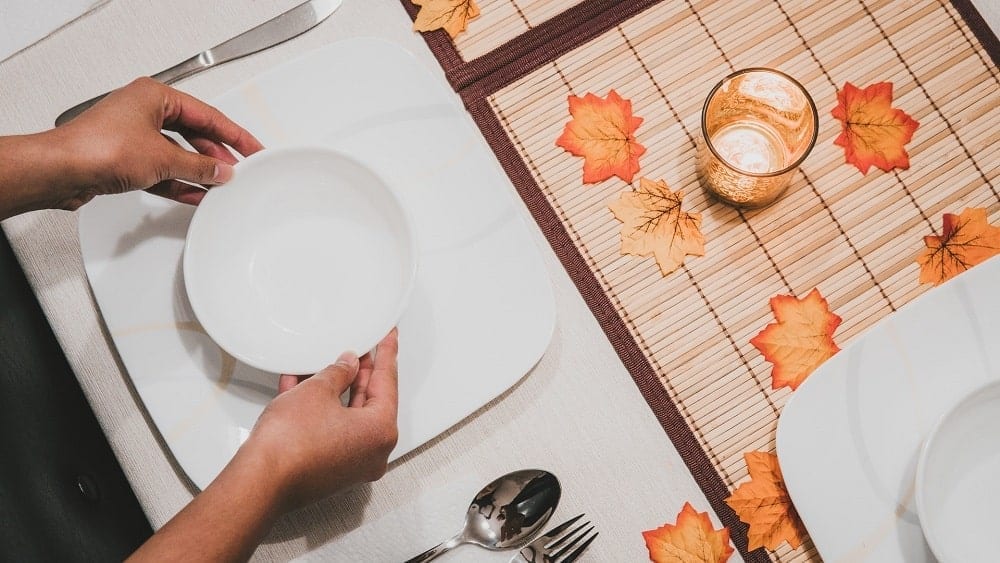 Close shot of white dish set next to bamboo placemat covered in orange leaves and an orange candle.