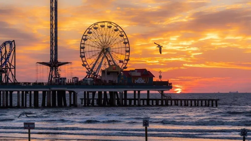 The sun setting behind a pier with a Ferris Wheel and other attractions.