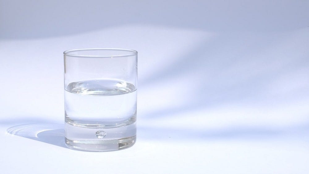 Glass of water half filled in front of a white and blue background.