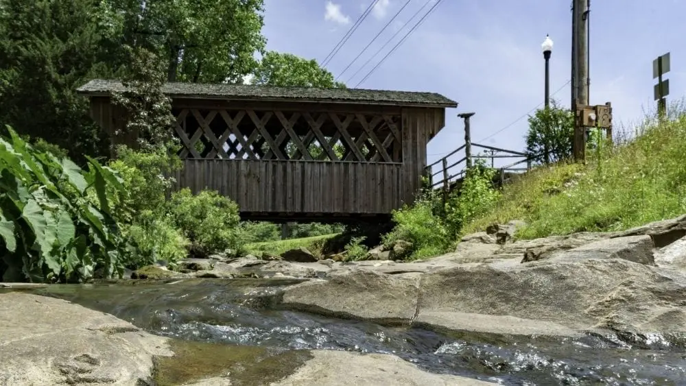 A small, historic covered bridge over a small creek that cuts through stones.