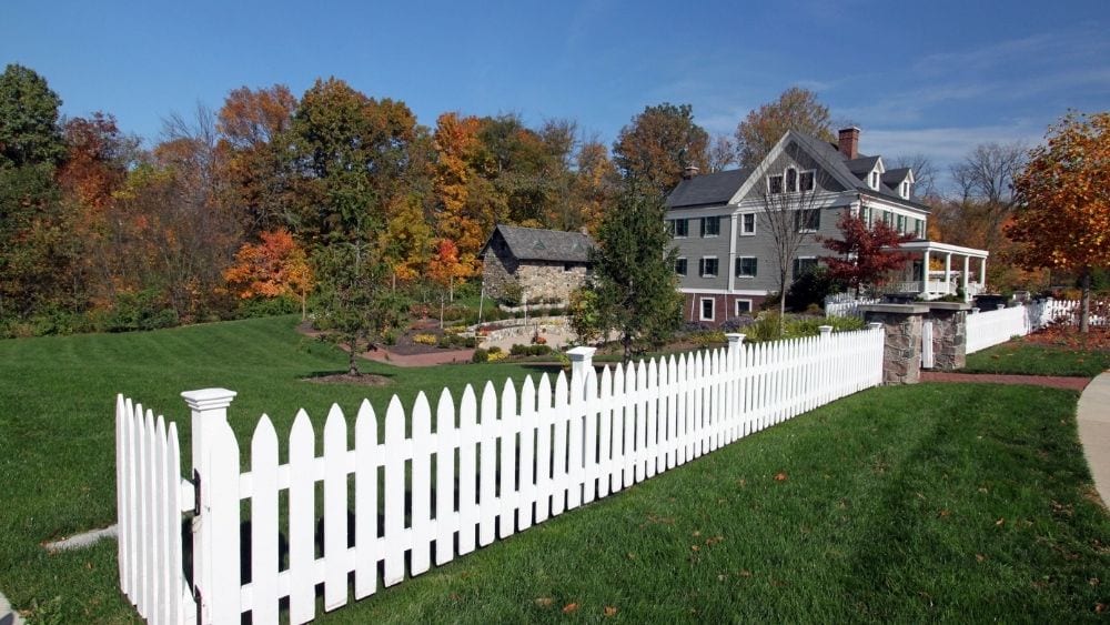 A stately 3-story home with a large yard and a white picket fence.