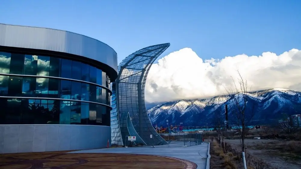 Modern metal and glass city aquarium with mountains and a clear sky in the background.
