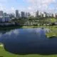 Aerial view of a lake surrounded by a well-maintained golf course. A city skyline stands in the background.