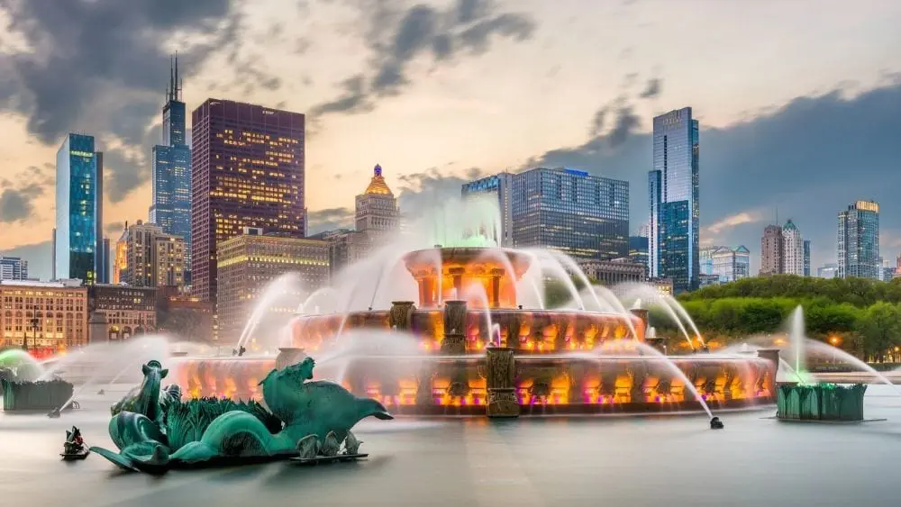 A grand fountain lit up in the evening with the Chicago skyline in the background.