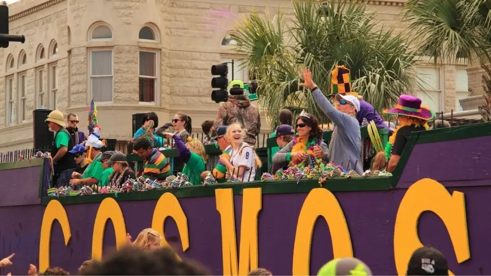 People waving and smiling on a purple and yellow parade float.