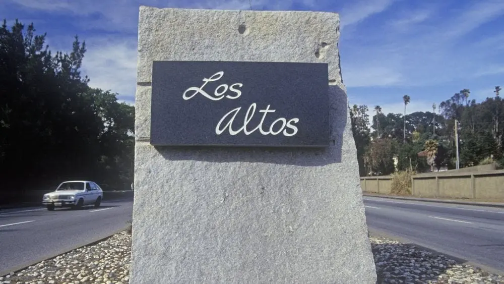 A metal sign etched with "Los Altos" written in cursive and mounted on a stone block.