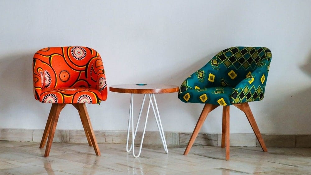 Two chairs with funky patterns and colors with a side table between them.