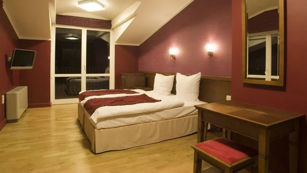 An elegant bedroom with maroon walls and hardwood flooring.