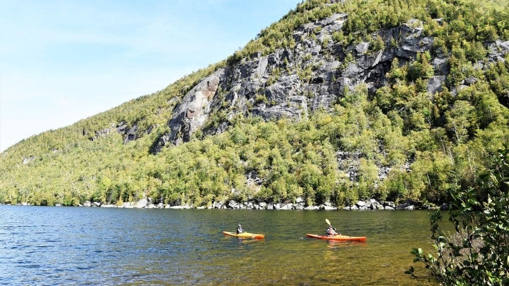 Kayakers in the water with a mountain in the background on a peaceful, clear day.