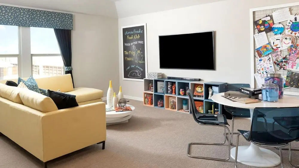 Kid's playroom with a small yellow couch, a TV, and a bulletin board filled with art.